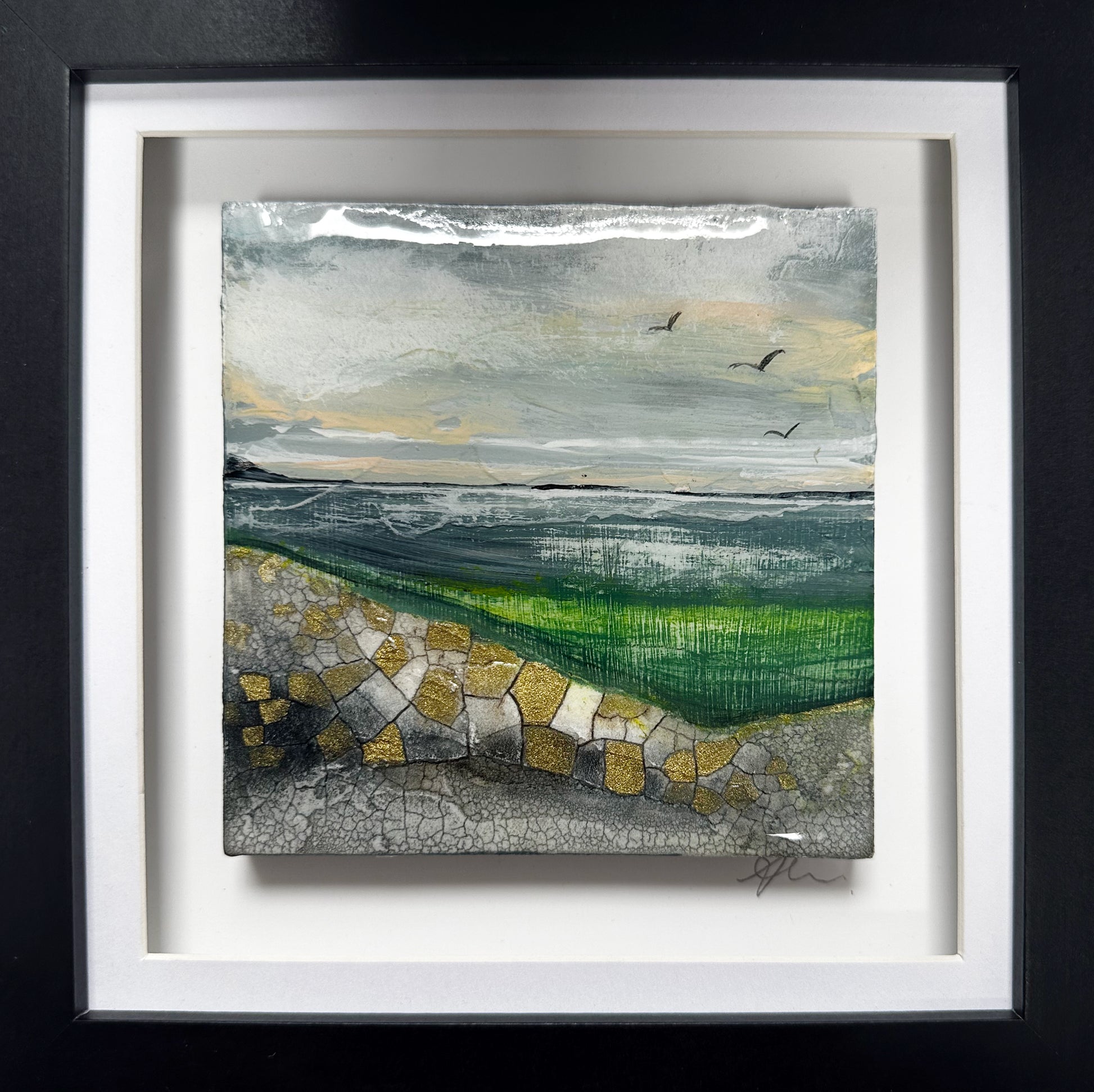 A framed landscape art print featuring a textured green field, a stone path in the foreground, and a cloudy sky with birds, presented in a white mat and black frame.