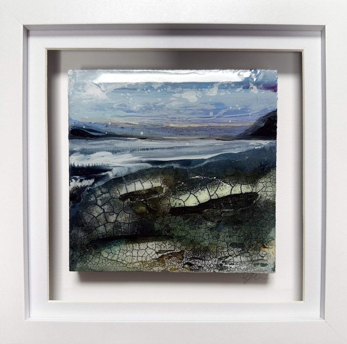 A framed landscape art print featuring a textured, cracked surface with blue, gray, and green tones, set in a wide white frame.