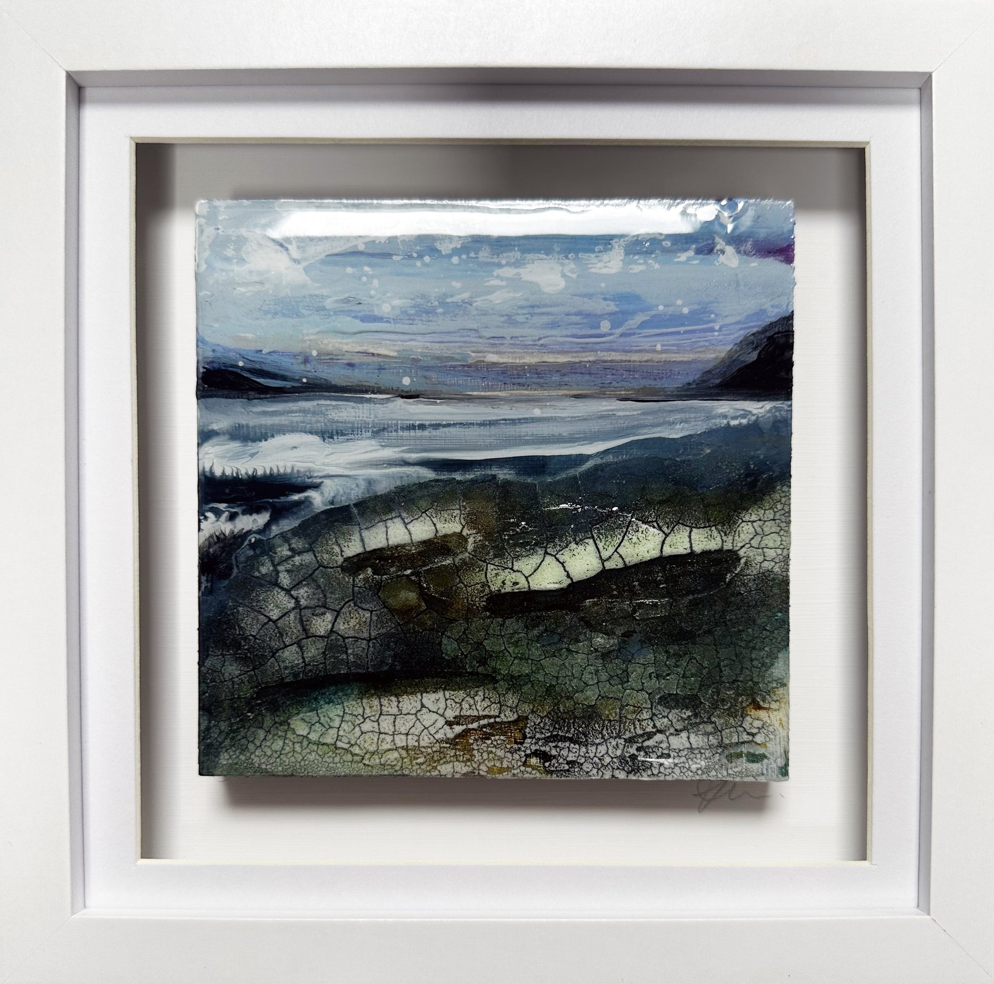 A framed landscape art print featuring a textured, cracked surface with blue, gray, and green tones, set in a wide white frame.